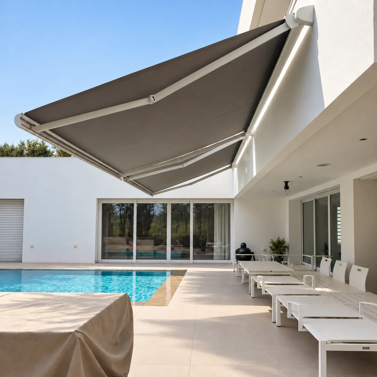 Store banne déployé au-dessus de la terrasse d’une villa avec piscine.